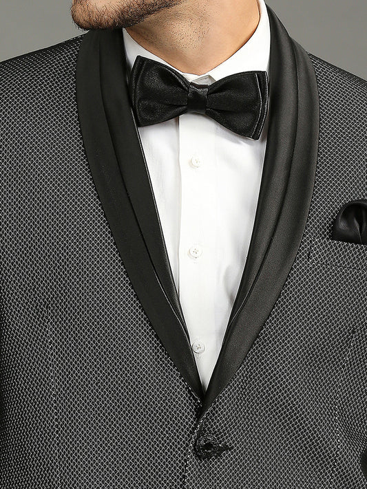 Close-up of a man wearing a black textured tuxedo jacket with satin shawl lapels, a white dress shirt, a black satin bow tie, and a black pocket square.