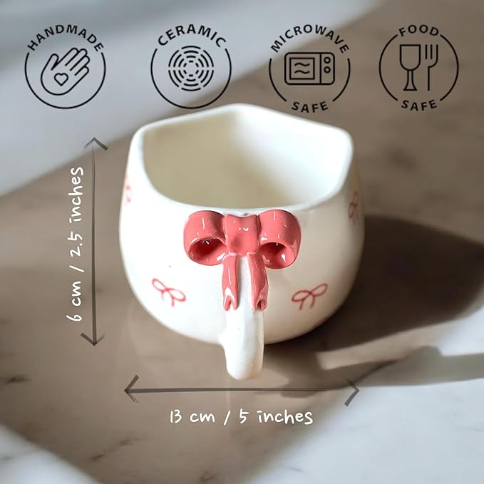 Ceramic mug with a pink bow design on a marble surface, showing safety and feature icons.