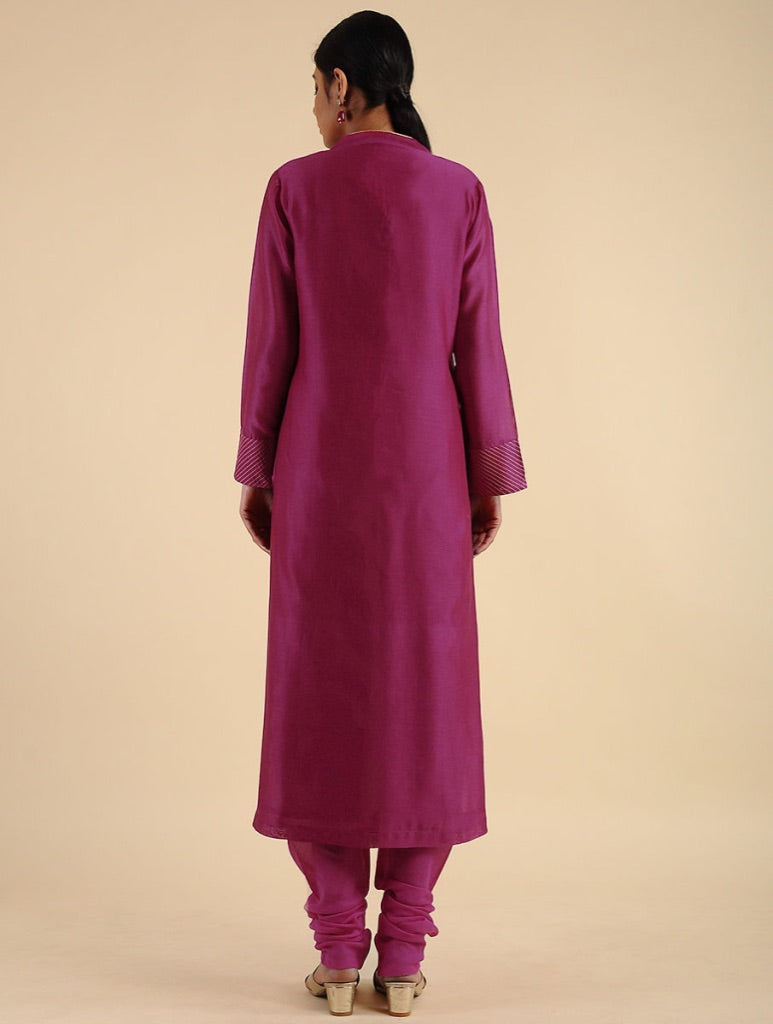 A woman viewed from the back wearing a magenta long kurta with matching pants, standing against a solid beige studio background.