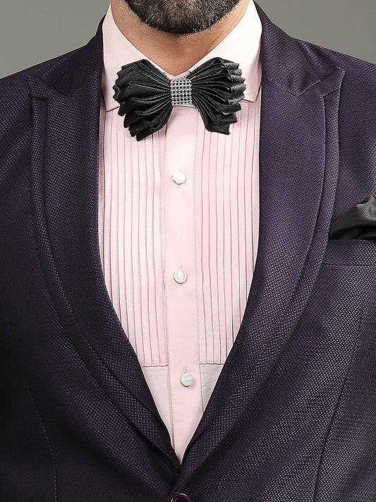 A close-up of a man's formal wear featuring a textured dark purple suit jacket, a light pink pinstriped dress shirt, and a black pleated bow tie with a silver rhinestone center.
