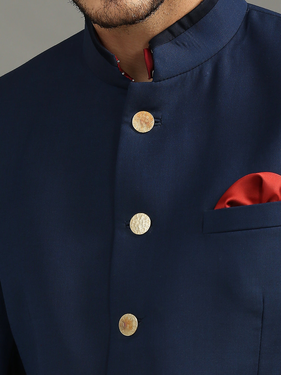 Close-up of a navy blue kurta with gold buttons, a red pocket square, and a mandarin collar.