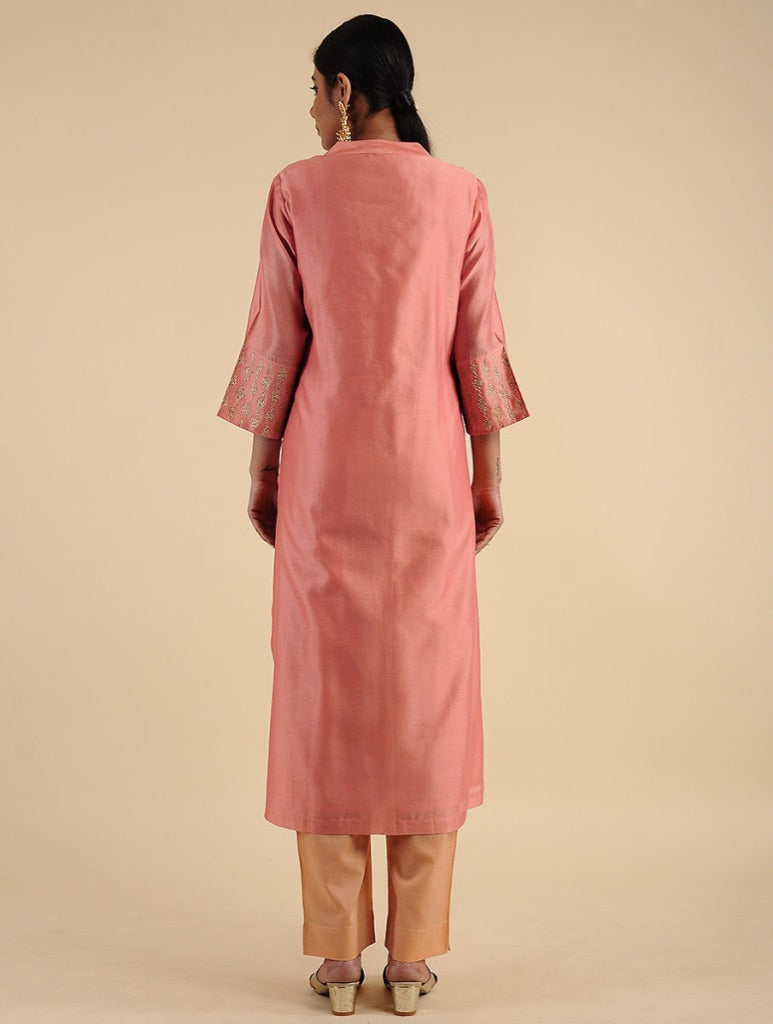 A woman shown from the back wearing a dusty pink long kurta with three-quarter sleeves and beige trousers, standing against a solid beige studio background.