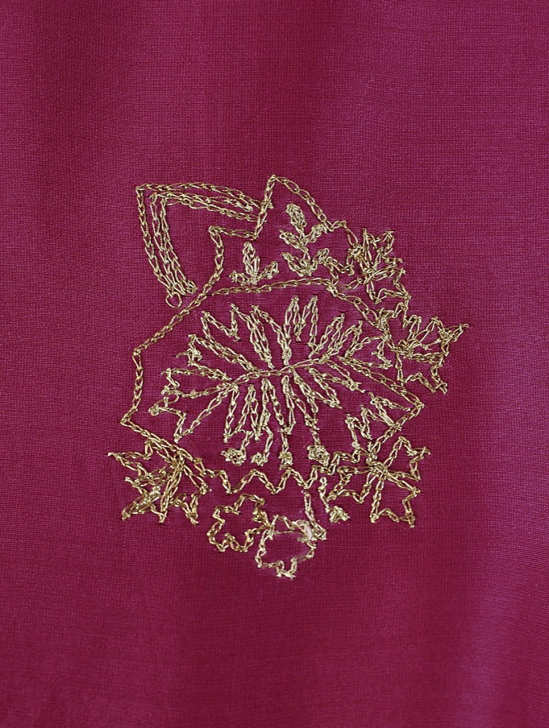 A close-up of a magenta fabric with a gold embroidered floral or paisley-like motif in the center.