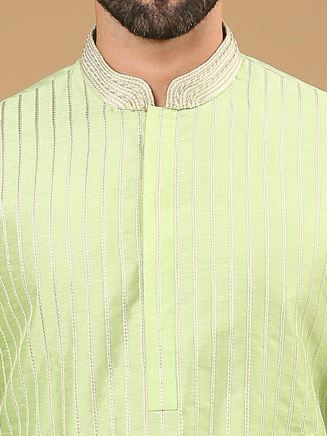 Close-up of a man wearing a light green kurta with vertical gold stripes and a decorative beige mandarin collar.