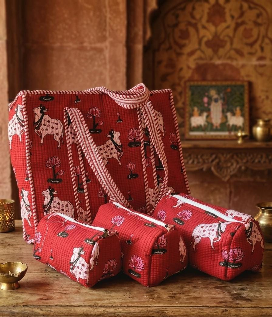 A matching set of red fabric pouches and a tote bag with a white and black spotted animal print, displayed on a rustic wooden table in a warm, traditional interior setting.