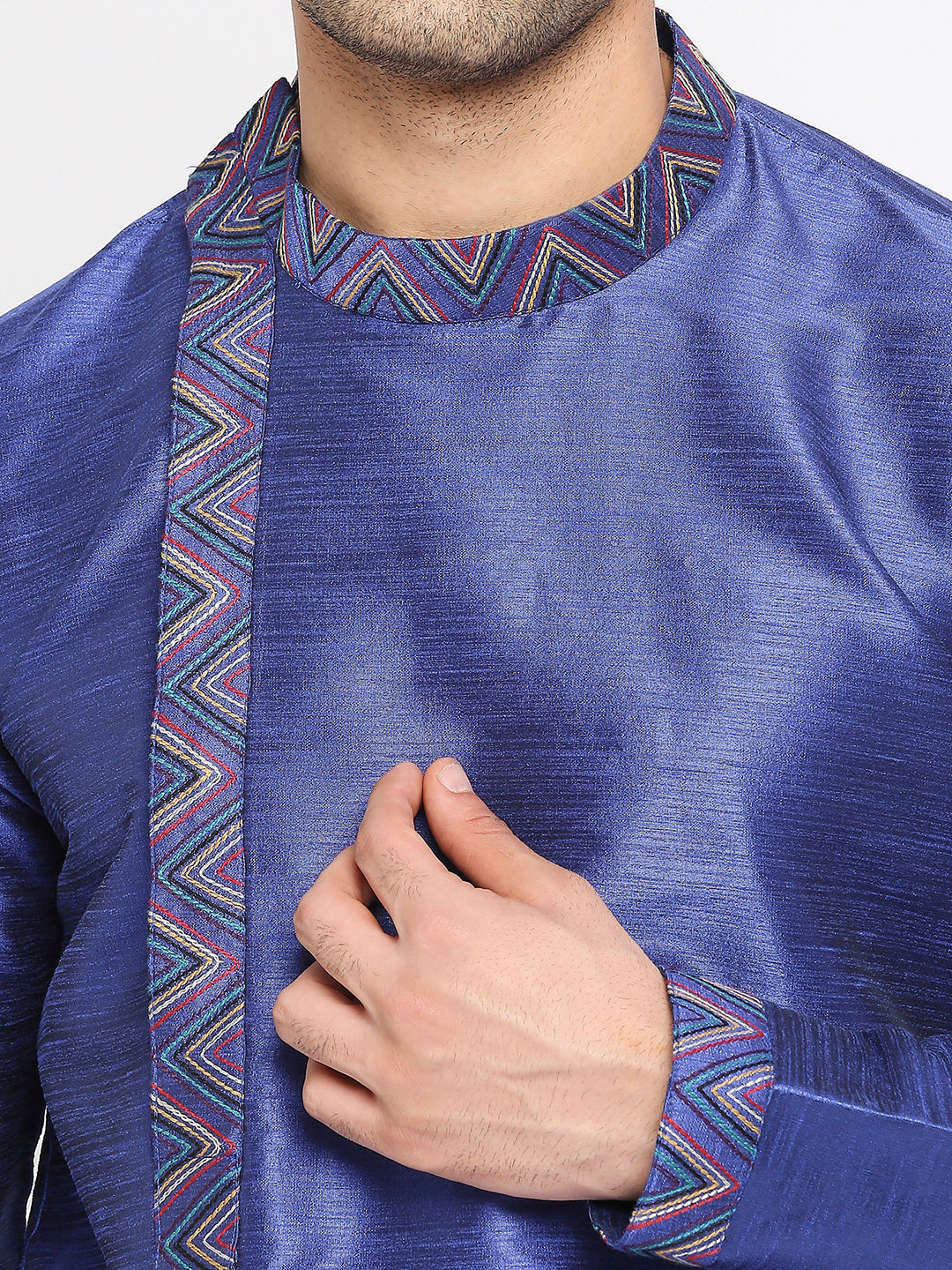 A close-up of a man wearing a blue traditional kurta with a colorful geometric patterned collar and vertical stripe detail on the chest.